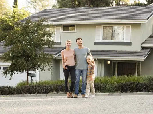 Mother, father and child standing in front of their home.