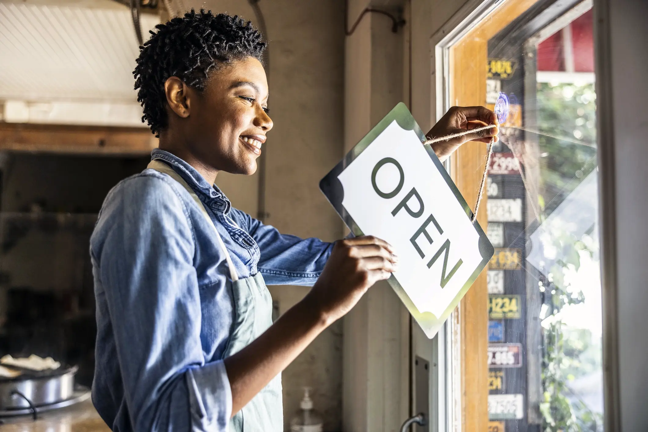 A small business owner flipping an "open" sign on a shop door, representing the importance of business insurance for protecting daily operation